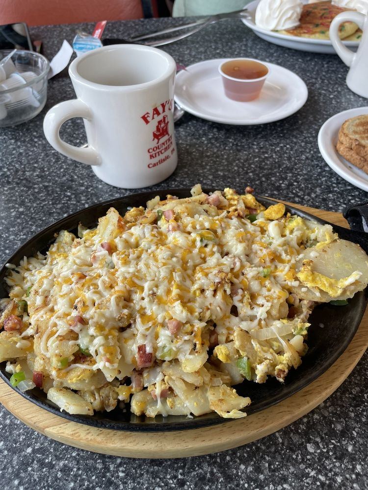 Western skillet with eggs, ham, peppers and melted cheese, next to a Fay's mug