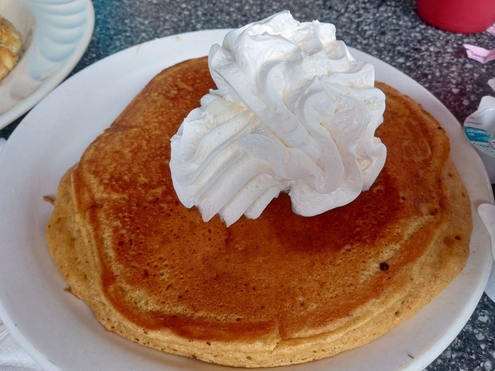 A plate-sized pancake topped with whipped cream